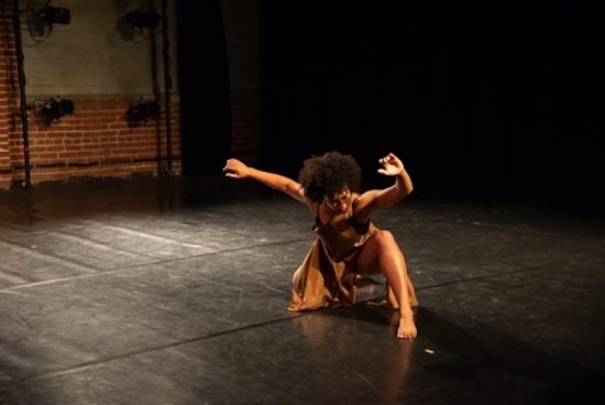 A woman has one knee on the ground and her hands in the air