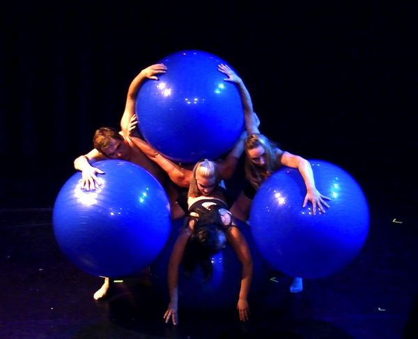 A group of dancers hold 3 giant blue balls