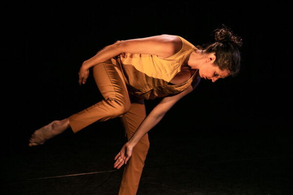 A dancer in brown bends forward