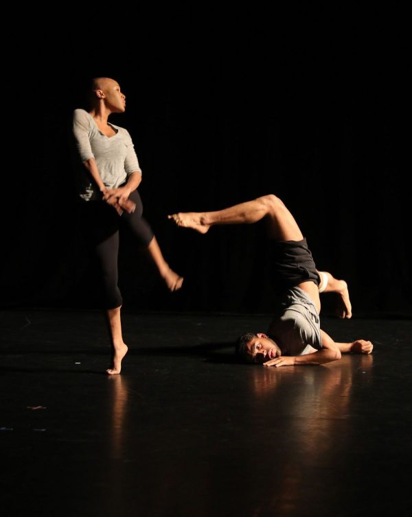 One dancer with a white shirt stands, another does a modified headstand