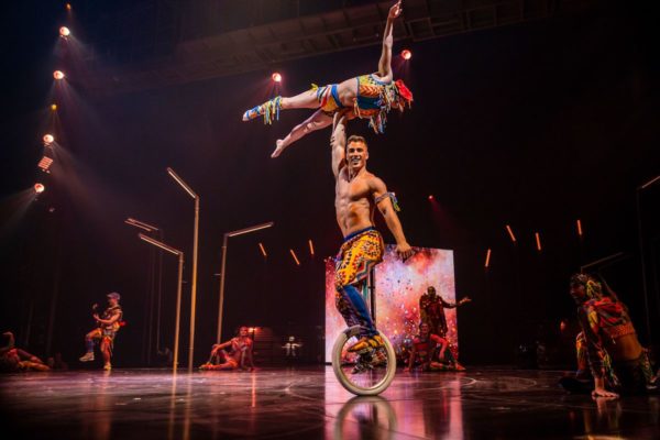 A man on a unicycle holds a woman above his head