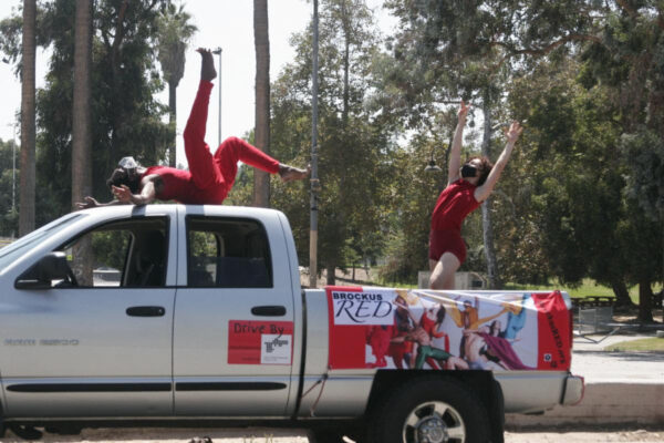 Two people in red outfits dancing on top of a gray pickup truck parked.