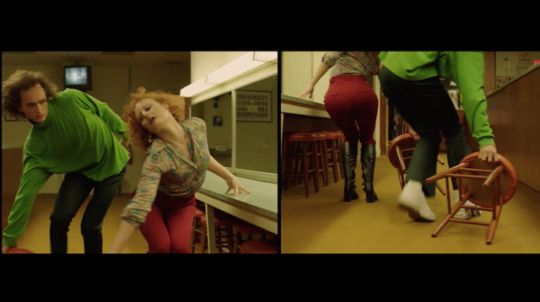 A split screen shot of a couple of dancers, one front view and one back view, dancing synchronized. He is wearing  green long sleeve top and black pants. She is wearing a beige blouse and red pants. They're both dragging stools.