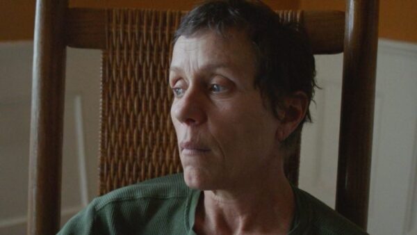 A medium shot of actress Frances McDormand wearing a green shirt, sitting on a wooden chair, from the film Nomadland.