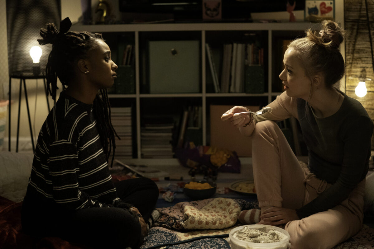 Two young women, one Black and one White, sitting on the floor face to face, serious looks on their faces.