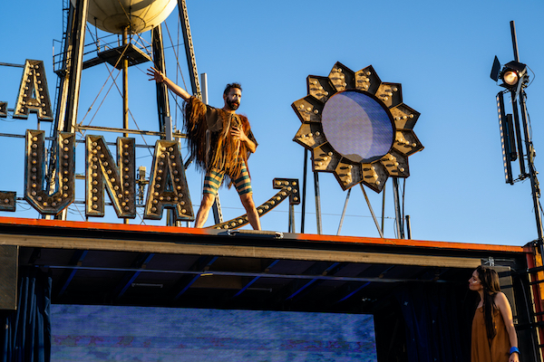 A man in striped bicycle shorts stands on top of a stage