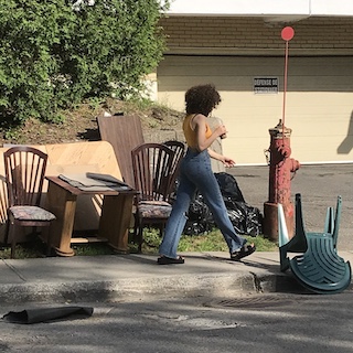 young lady walking by abandoned furniture on the sidewalk