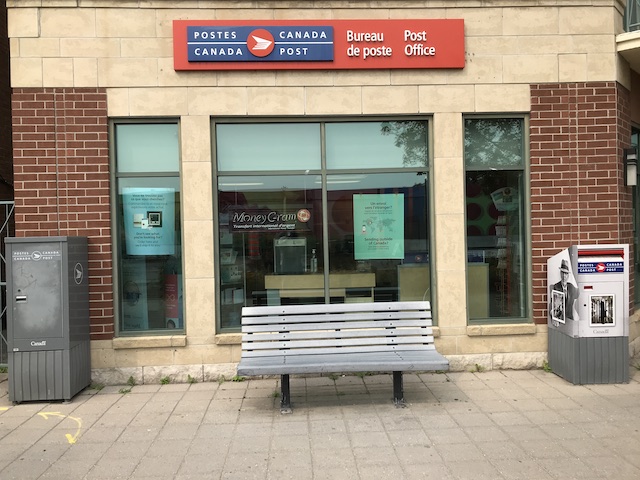 single bench associated with postal service framed by mail boxes easily identified with Canada Post