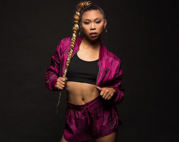 A female dancer with a long braid poses in bright raspberry shorts and jacket