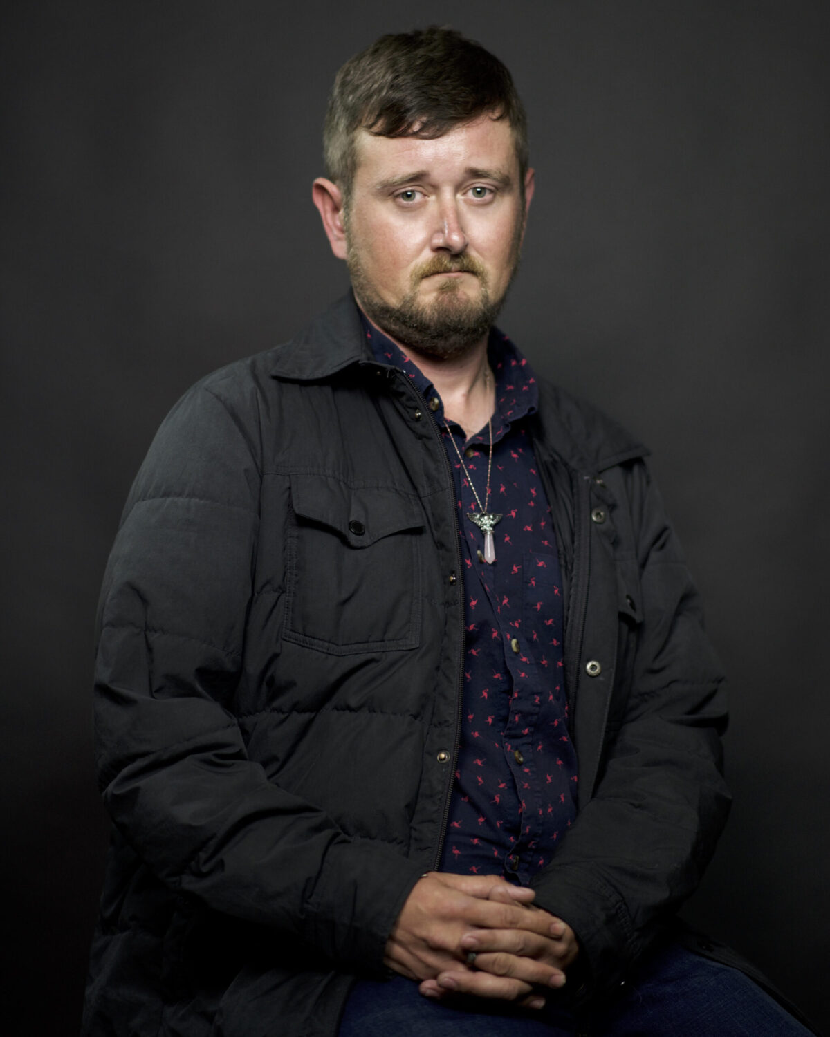 A photo of poet Kevin Ridgeway looking at the camera. He is not smiling. His eyes look somewhat sad.