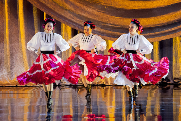Three female dancers in white blouses and red, ruffled skirts.