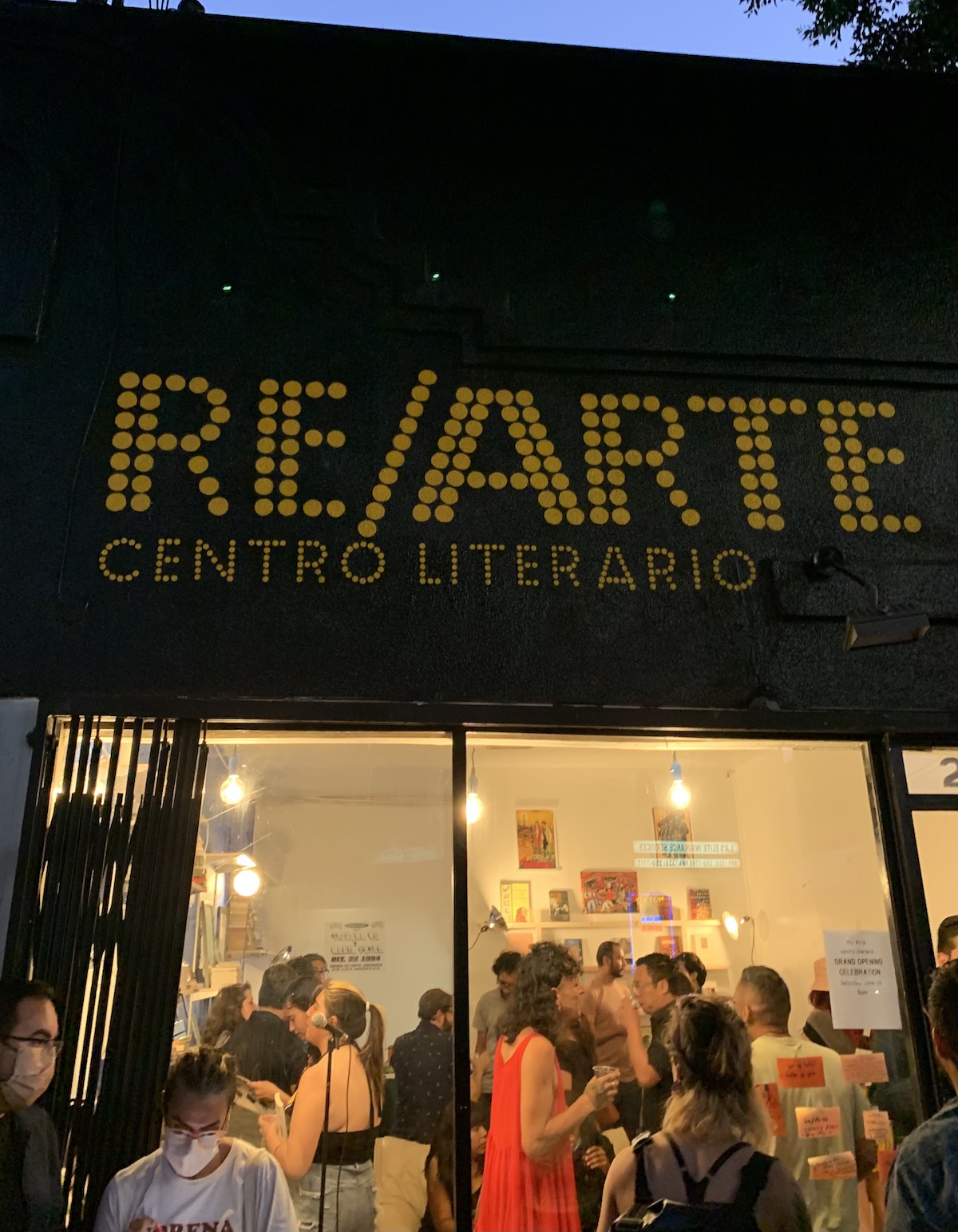 Sign reads RE/ARTE, Centro Literario outside a storefront, with a crowd enjoying themselves inside.