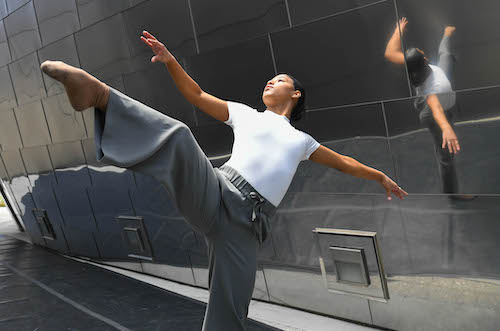 A woman dances reflected in Disney Hall behind her