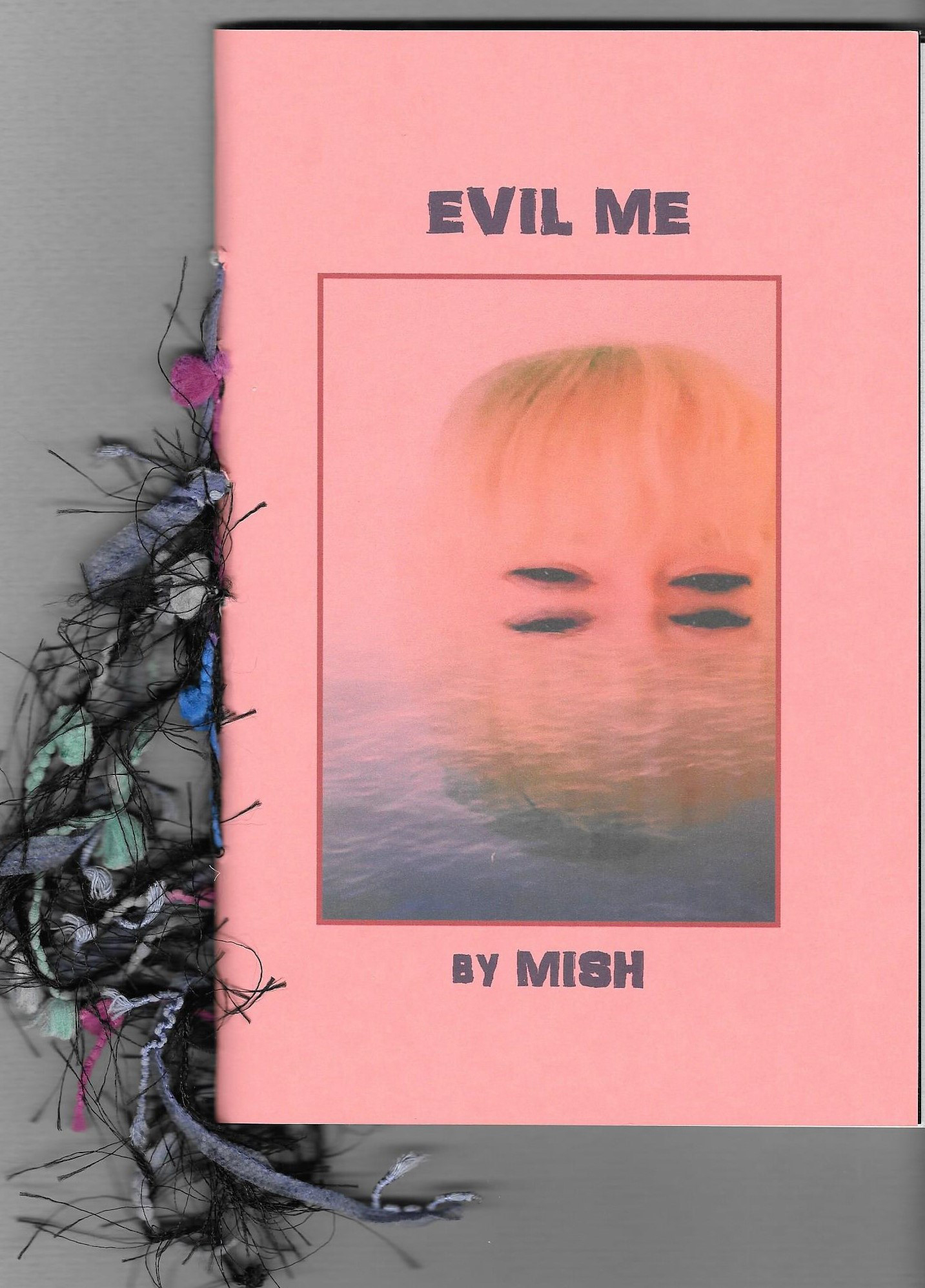 Cover of Evil Me, a chapbook by Mish, is salmon colored background and image of a woman's face underwater up to her eyes; the reflectionin the waterz makes it look like she has 4 eyes