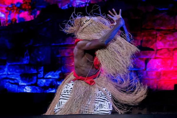 A heavily muscled male dancer with long brown grass over his face