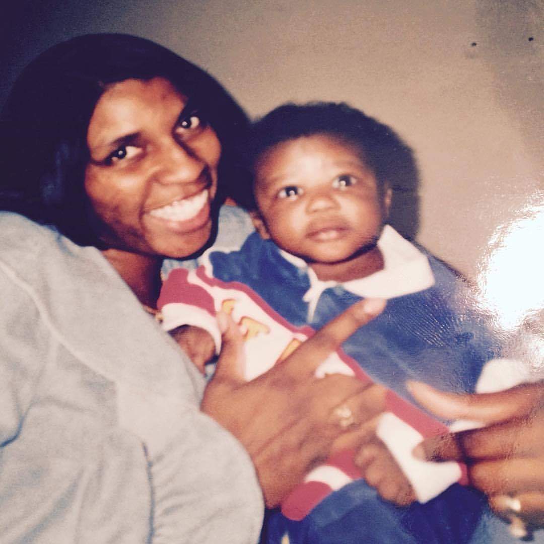 A beautiful Black woman with a giant smile on her face holds a baby boy to her chest.