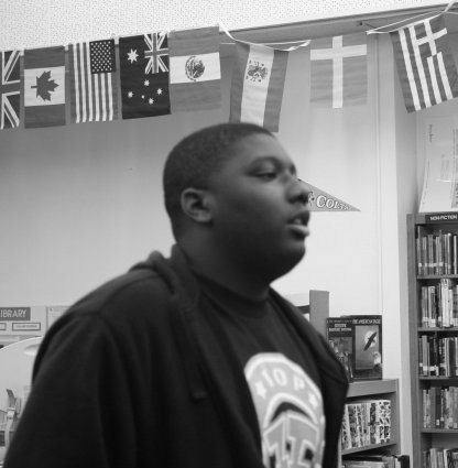 A young Black man up speaking in from of a row of flags from different countries