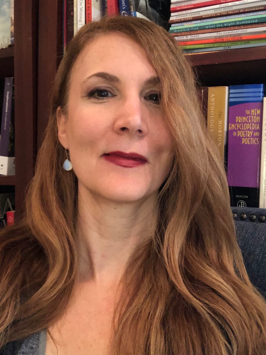 Headshot of poet Neese Tayve. She has long strawberry beautiful hair, red lips, and teal earrings. She looks comfortable and confident.