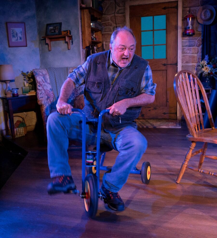 From The Children, an older man rides around on a tricycle inside his home.