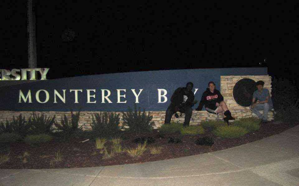 Chris Siders and two friends sitting in front of the Monterey Bay sign, covering the AY.