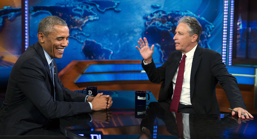 A screenshot of Barack Obama laughing as Jon Stewart gesticulates with his hands.