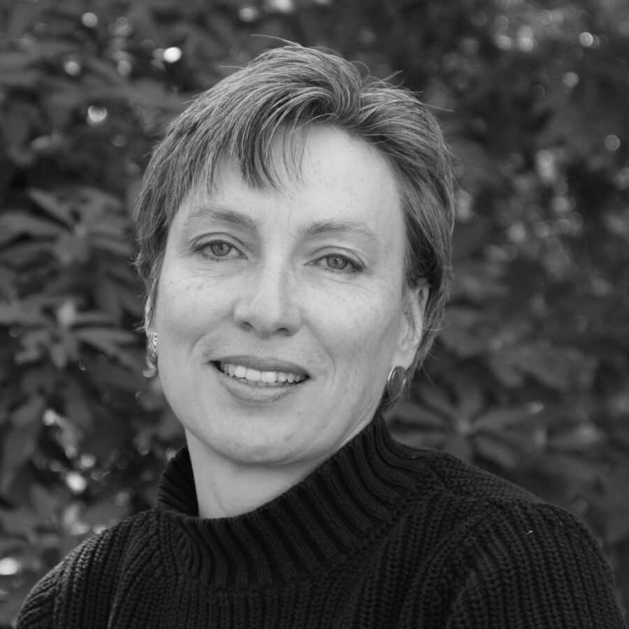 Black-and-white photo of poet Marilyn McCabe. She's in a black sweater, short hair parted to her right, with earrings, and smiling.