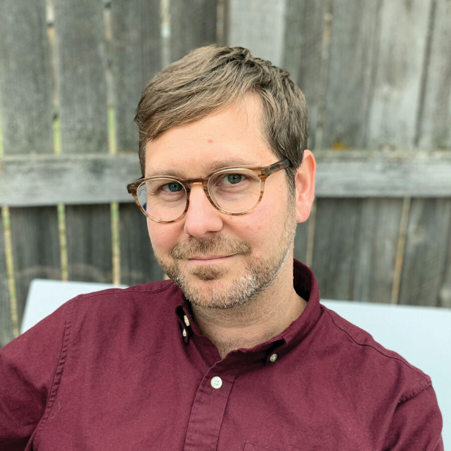 Photo of poet and professor Wayne Miller. He's in a maroon shirt, with glasses, staring at the camera.