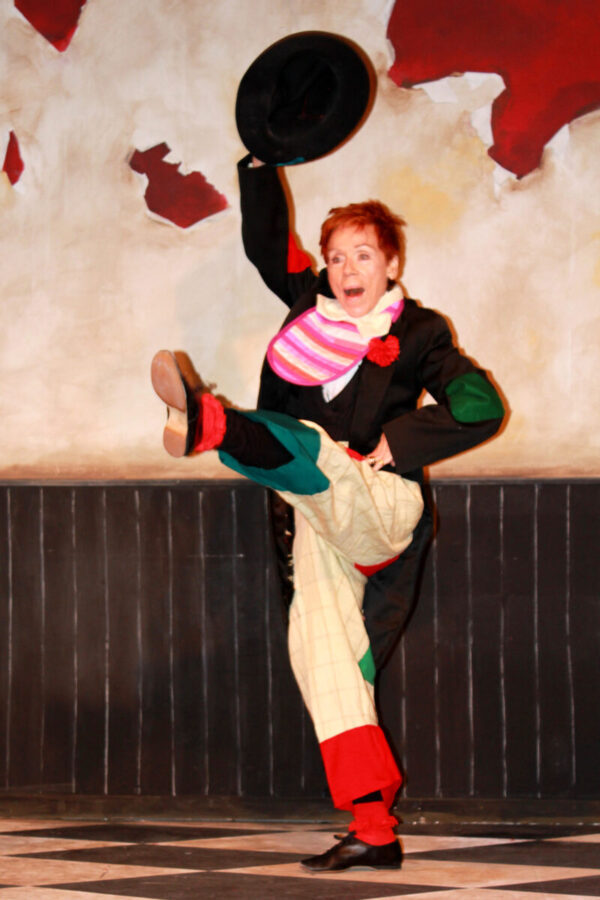 A woman lifts a hat while she kicks her leg