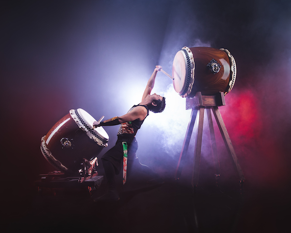 A Japanese drummer bends back to simultaneously play a drum in front and behind him