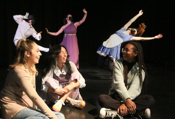 three actors sit in front of several dancers