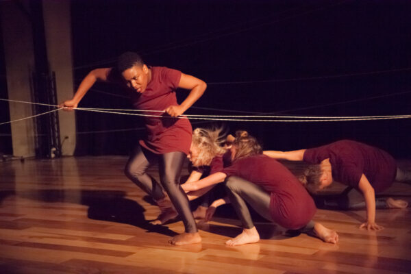 A group of women dancers in dark red hold a rope