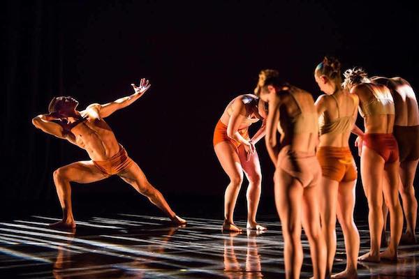 A man reaches back to a line of dancers