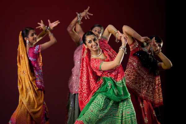A woman in a red and green sari dances with other women