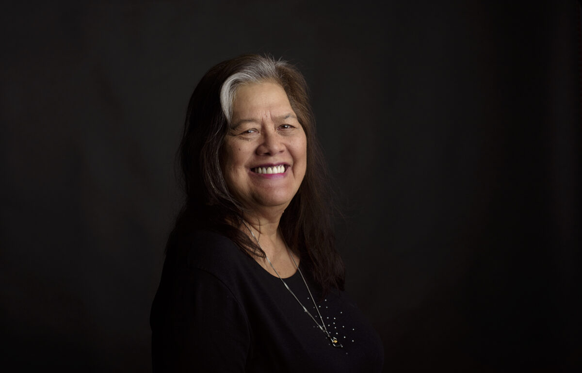 A professional photograph of Singaporean Eurasian poet Hedy. The background is black; Hedy is turning and smiling brightly at the camera.