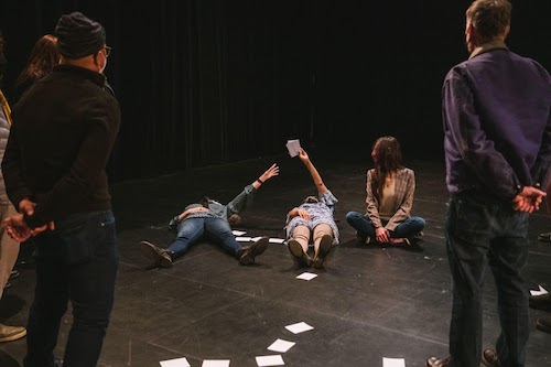Three people are on floor with two standing and watching