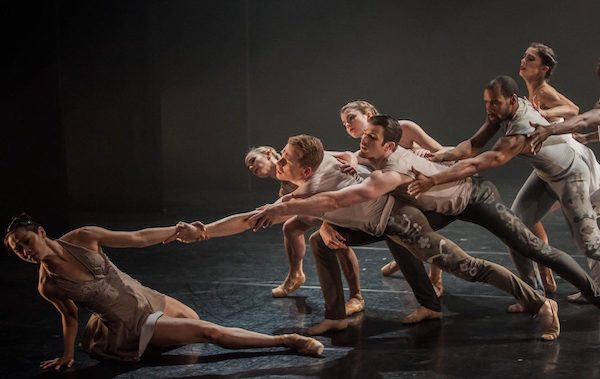 A group of dancers lean toward a dancer on the floor