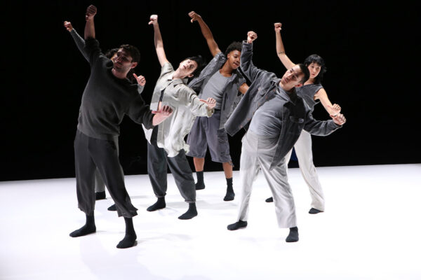 A group of dancers tilt downstage