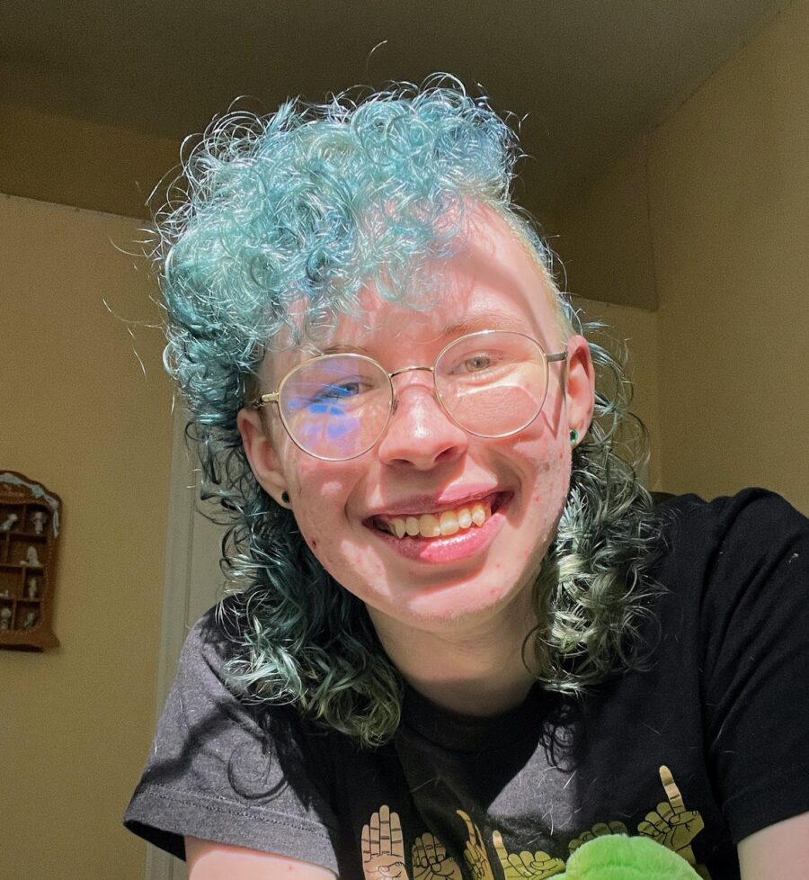 the author, Clay Johnson, with light blue hair and glasses, smiling in the sunlight coming into their room