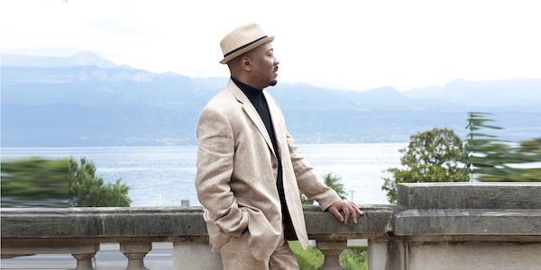A man in a white hat and coat looking out at water
