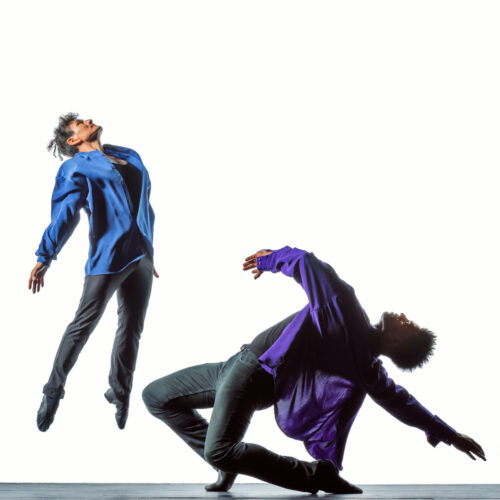 One male dancer jumps and one dance bends backwards