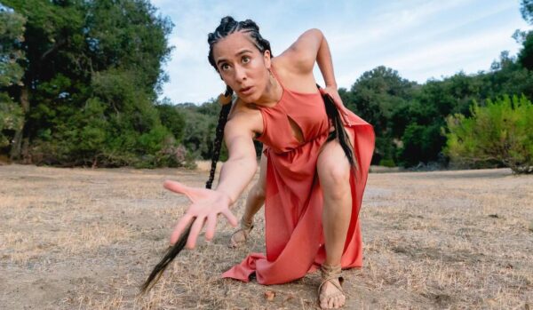 A dancer in red reaches her hand toward the camera
