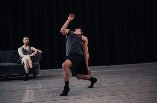 A female dancer bends back in front of a man on a sofa