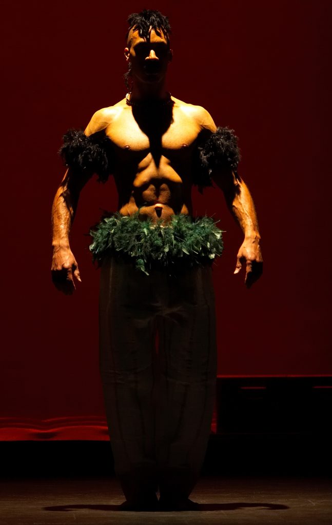 A bare chested man faces the camera