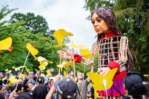 A tall puppet with a crowd holding paper butterflies