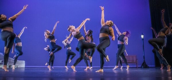 Dancers in black lift their arms