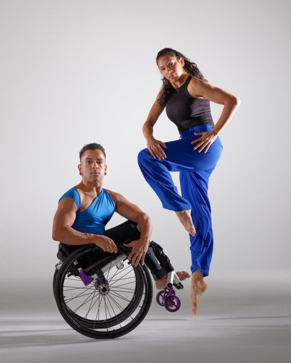 A dancer jumps by a dancer in a wheelchair