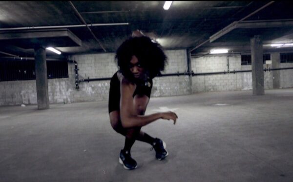 A dancer in a bare room leans forward
