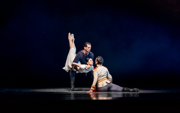 A dancer holds a dancer toward a kneeling man