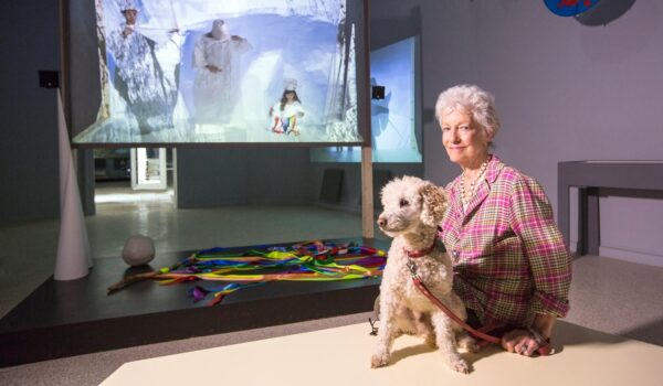 A woman sits with a dog in front of a painting