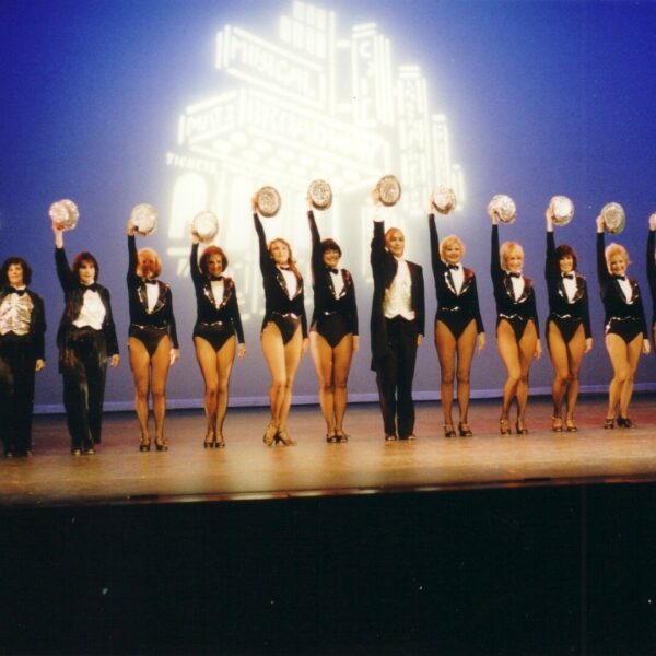 A line of dancers raise their hats